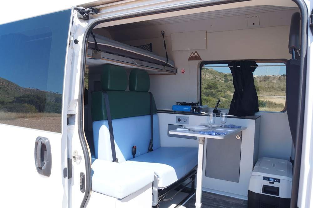 Mesa puesta dentro de la camper con la puerta lateral abierta
